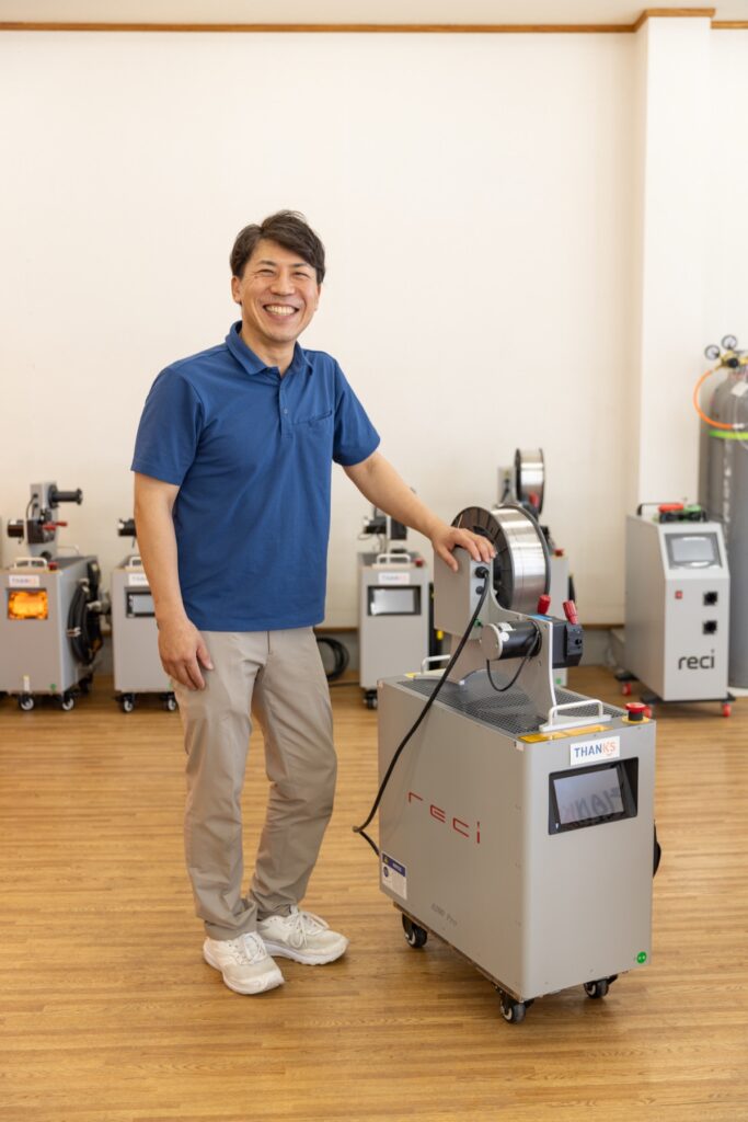 ファイバーレーザー溶接機の前に立つサンクス製作所の代表